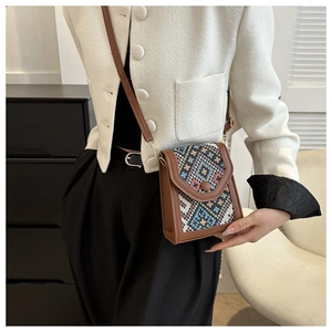 Gros plan d'un sac bandoulière en cuir marron à motif ethnique porté sur une veste blanche