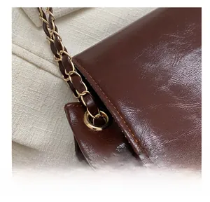Détail de la chaîne dorée et du cuir brillant marron foncé sur le sac fourre-tout