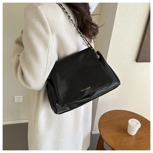 Détail du sac bandoulière en cuir noir avec lettrage doré porté par un mannequin