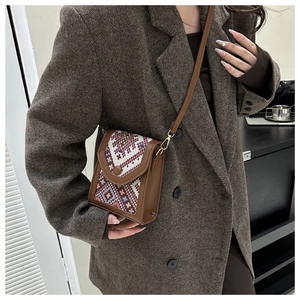 Détail d'un petit sac bandoulière vintage marron avec motif tissé sur un modèle en tailleur