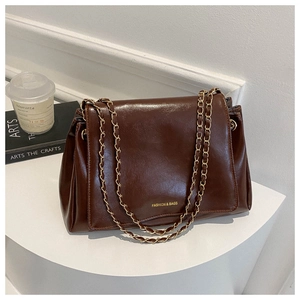 Détail d'un sac cabas marron foncé avec chaîne dorée sur un support blanc élégant