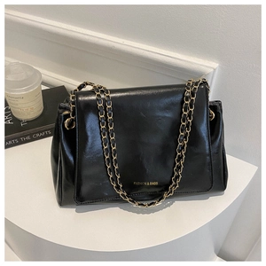 Détail d'un sac cabas en cuir noir brillant avec bandoulière chaîne dorée sur socle