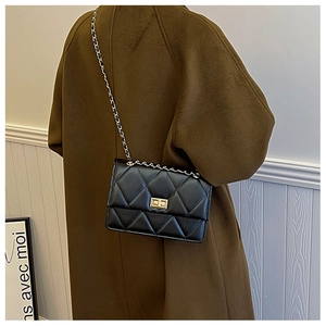 Klassische schwarze Stepptasche aus Leder mit goldener Schließe am Wollmantel