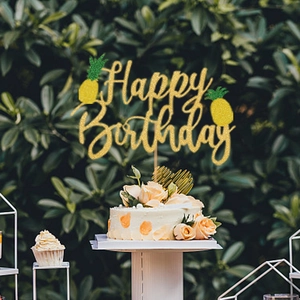 Close-up of golden glitter Happy Birthday cake topper with pineapple detail on white cake