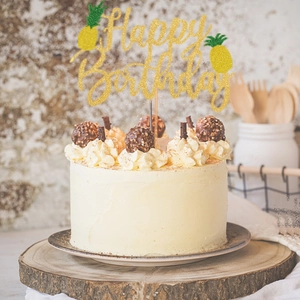 Close-up of glitter Happy Birthday cake topper with pineapple detail on white cake