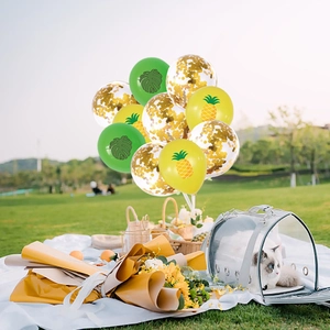 Macro shot of pineapple and palm leaf printed balloons with golden confetti accents