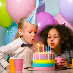Children wearing holographic mermaid party hats while celebrating at a birthday cake table