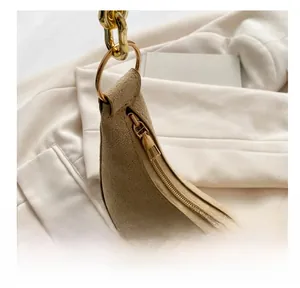 Detail of smooth metal zipper and gold chain on khaki suede crescent shoulder bag