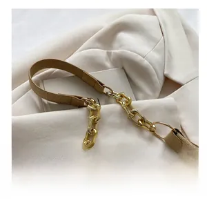 Close-up of textured golden metal chain and khaki suede strap on a crescent bag