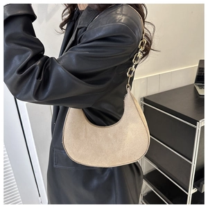 Detail of light beige suede crescent bag with metal chain strap worn on shoulder