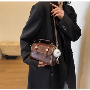 Detail of dark brown glossy leather handbag with gold buckles and plush charm on black suit
