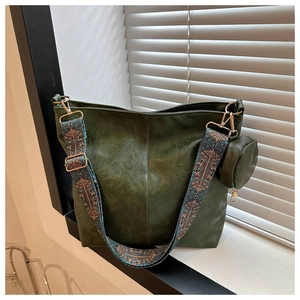 Close-up of a dark green leather tote with a colorful embroidered wide shoulder strap