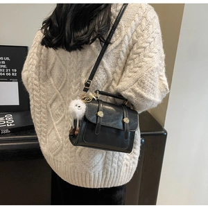 Close-up of black retro square bag with golden buckles and a white plush keychain