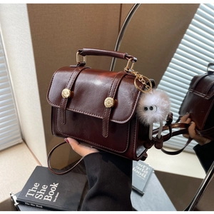 Close-up of a retro brown crossbody bag with gold hardware and a fluffy monster charm