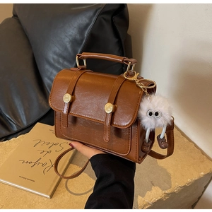 Detail of a brown vintage square handbag with a gold clasp and a white plush charm