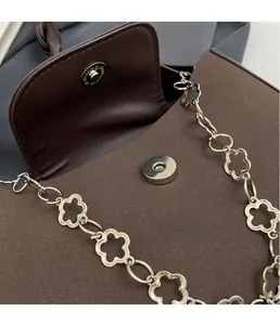 Close-up of matte dark brown leather bag with silver floral chain and magnetic buckle