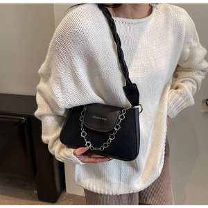 Detail of black leather bag featuring silver flower chain and logo on white sweater
