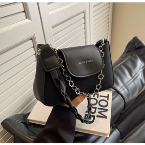 Detail of black leather shoulder bag featuring silver flower chain and woven handle