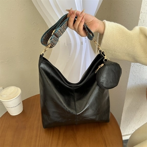 Black leather hobo bag with patterned wide strap and mini round pouch on wooden desk