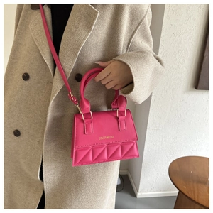 Close-up of quilted magenta PU leather crossbody bag with top handle on a beige coat