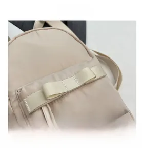 Close-up of beige nylon mini backpack featuring a ribbon bow and drawstring zipper pull