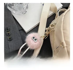 Pink furry monster bag charm with large eyes and boots hanging on a beige backpack