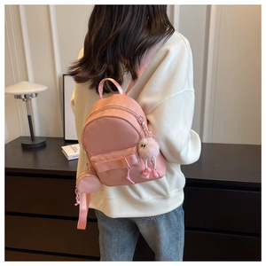 Close-up of mini pink backpack with bow detail and plush ball charm on model