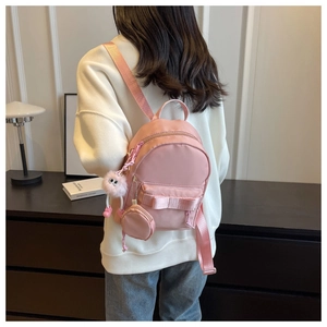 Detail of pink bow backpack with plush monster pendant and mini coin purse accessory