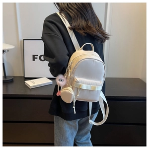 Mini cream nylon backpack featuring a round coin purse and pink plush doll charm