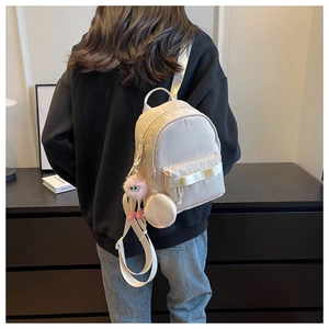 Mini cream nylon backpack with bow detail and pink plush monster charm on model