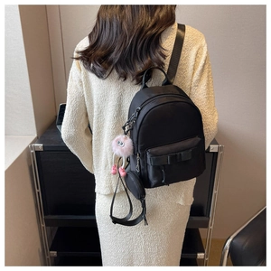 Close-up of black bow-knot backpack with pink monster plush charm and mini round purse
