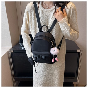 Mini black backpack for women with bow decoration, plush charm, and coin purse on model