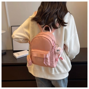 Detail of pink mini backpack featuring a plush charm and small round coin purse accessory