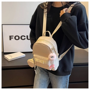 Mini beige backpack with bow detail and pink furry pendant on a black sweater model