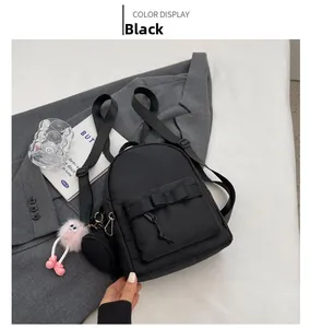 Detail of black nylon mini backpack with a ribbon bow and pink plush monster charm accessory