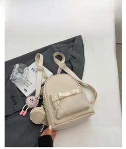 Close-up of a cream mini backpack with bow detail and plush charm on a grey suit jacket