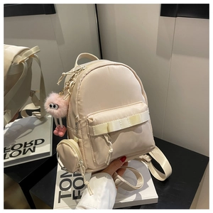 Detail of beige nylon backpack with small round pouch and pink plush monster pendant