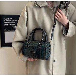 Detail of green plaid crossbody bag with black leather straps and gold metal plaque