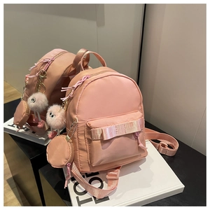 Detailed view of pink nylon mini backpack with a fluffy charm and small coin purse accessory