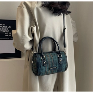 Detail of vintage plaid cylinder bag with leather handles shown on a beige coat
