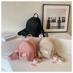 Detailed display of mini bow backpacks in black, pink and beige with plush pompom charms