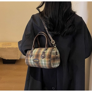 Detail of plaid wool cylinder bag with dark brown leather straps and gold hardware accent