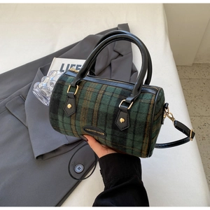 Detail of green plaid cylindrical pillow bag with leather handles and fashion label