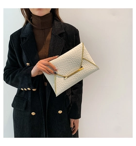 Dettaglio della pochette a busta bianca intrecciata con bordo dorato per un look chic