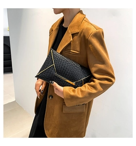 Dettaglio di una pochette a busta in pelle nera intrecciata con eleganti bordi dorati