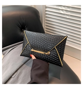 Dettaglio di una pochette a busta nera intrecciata con hardware dorato tenuta da modella