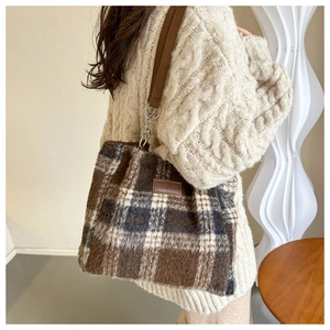 Detail of wool plaid tote bag featuring brown leather straps and embossed fashion tag
