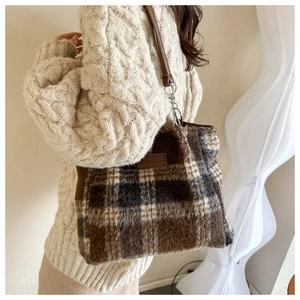 Brown plaid wool tote bag with leather strap and fashion patch on warm backdrop