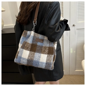 Detail of wool bucket bag showing blue and brown plaid pattern with leather shoulder strap