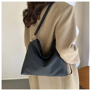 Side view of a black hobo shoulder bag with matte texture on a camel wool blazer